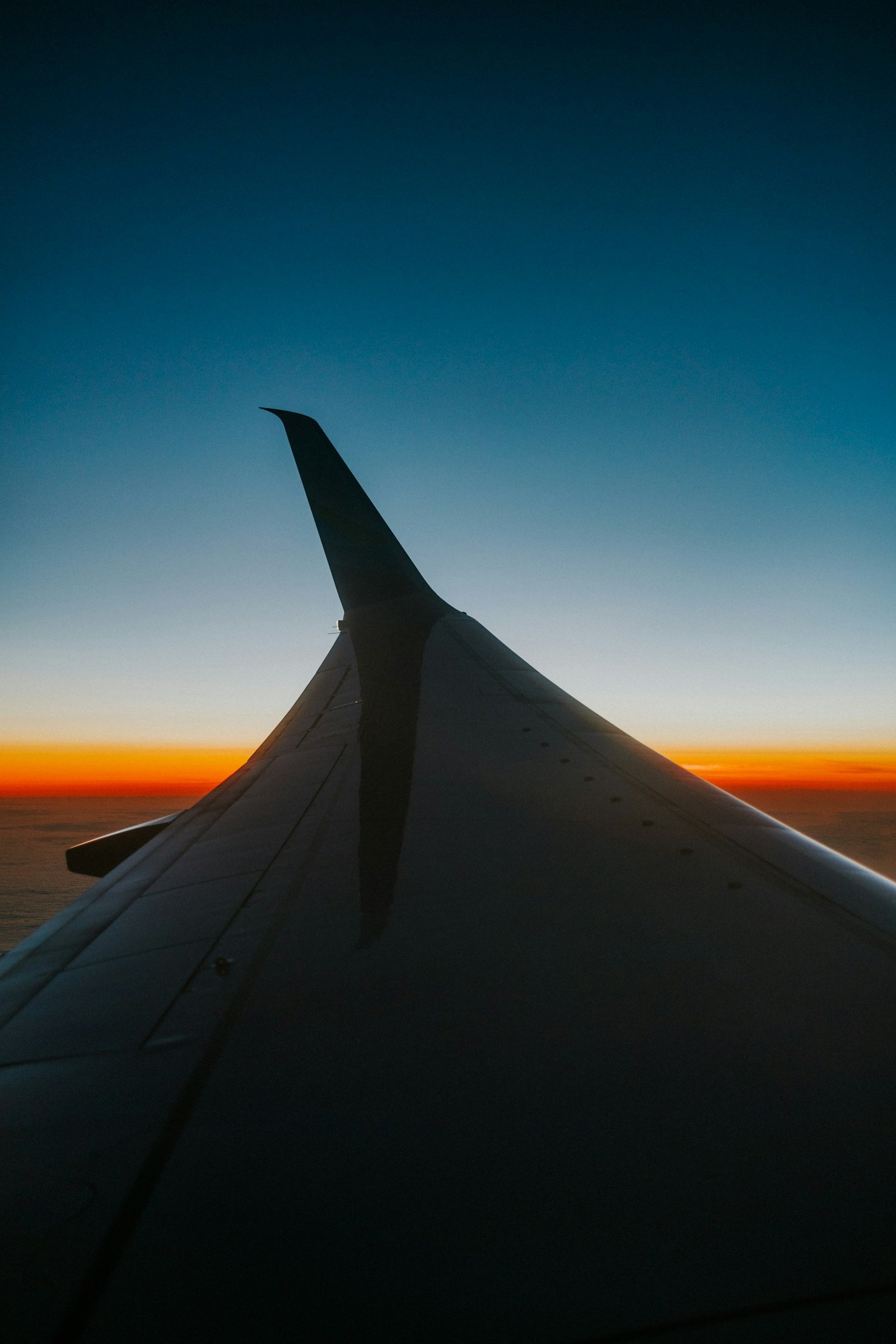 An aircraft wing silhouetted against an orange sunset from a passenger window.