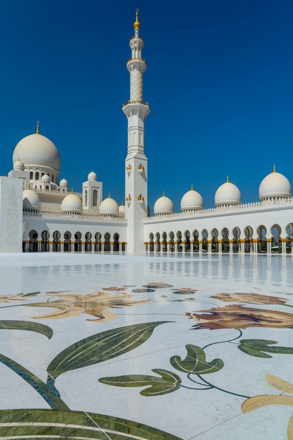 The white domes and a minaret of the Sheikh Zayed Grand Mosque in Abu Dhabi, seen across its marble courtyard.