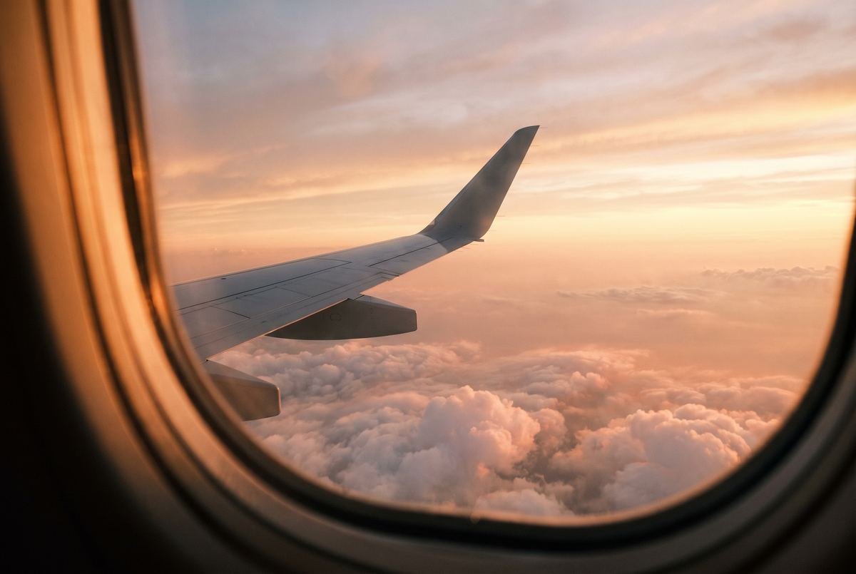 The view over an aircraft wing above the clouds at sunset.